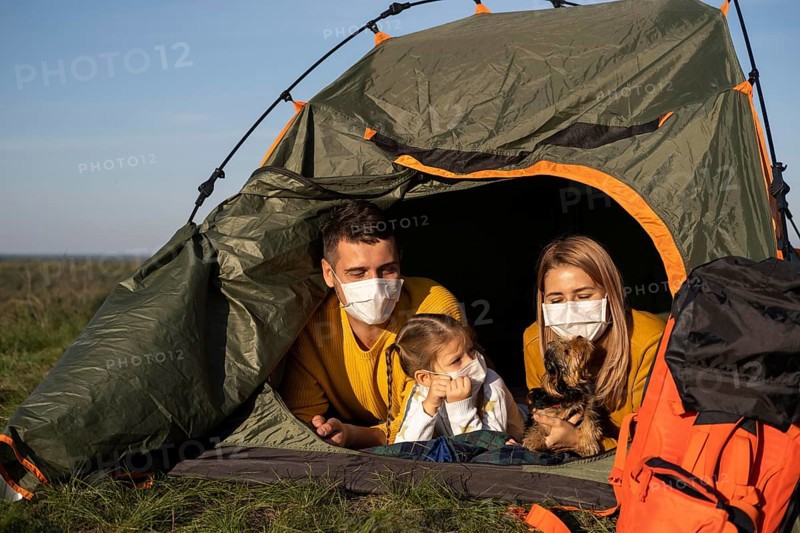 Family wearing masks sitting tent with their dog front view