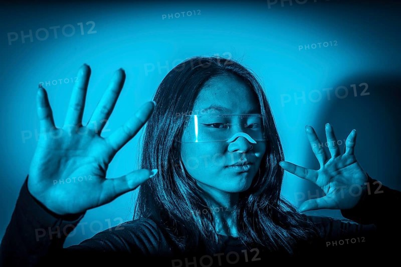 Studio photo with blue background with neon lights of chinese woman gesturing while wearing augmented reality goggles