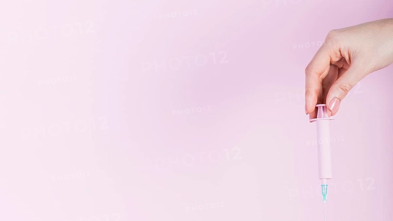 Human hand holding plastic syringe pink backdrop