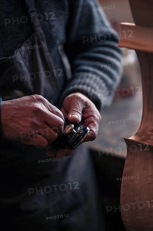 Senior violinmaker wrinkled old hands holding a tool chisel in workshop in Cremona