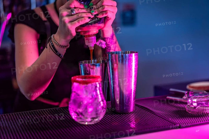 Bartender mixing ingredients in a cocktail mixer in the counter of a bar with neon lights