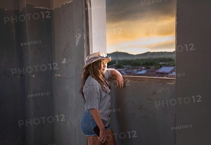 Young woman tourist looking at the sunset through an old window in Granada