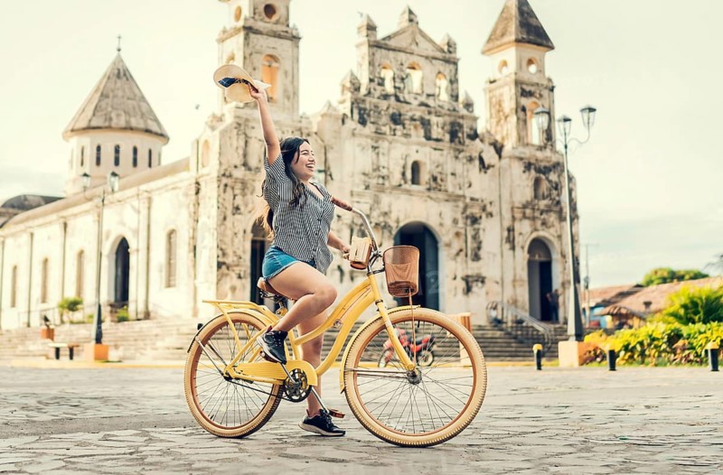 Lifestyle of a happy girl riding a bicycle holding her hat on the street. Happy young woman in hat riding a bicycle on the street. Granada