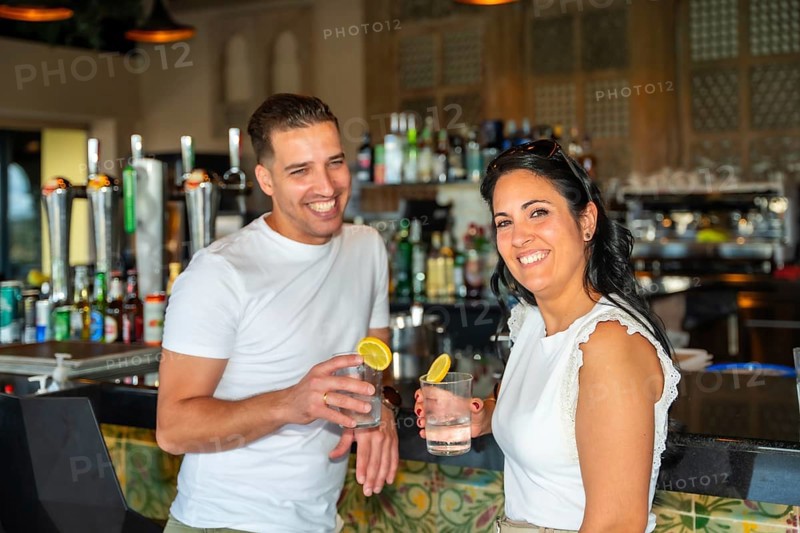 Horizontal portrait of a caucasian couple smiling at camera drinking cocktails in a luxury bar