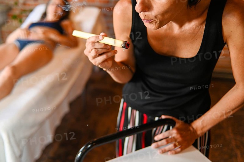 Therapist prepare burning mugwort or moxa herb to apply to 50s adult fit caucasian female patient to facilitate healing and blood flow