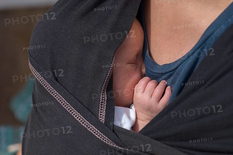 Baby sleeping in a sling with his mother