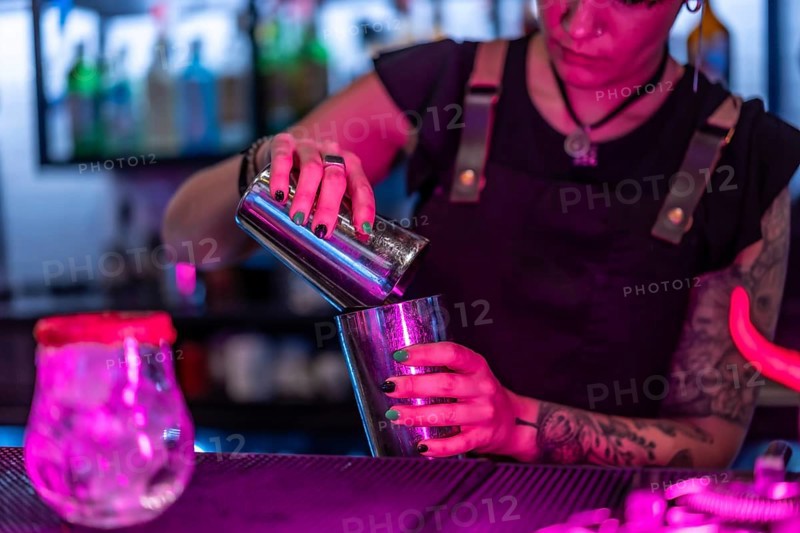 Close-up with focus on a female waiter mixing ingredient preparing a cocktail in the counter of a bar at night