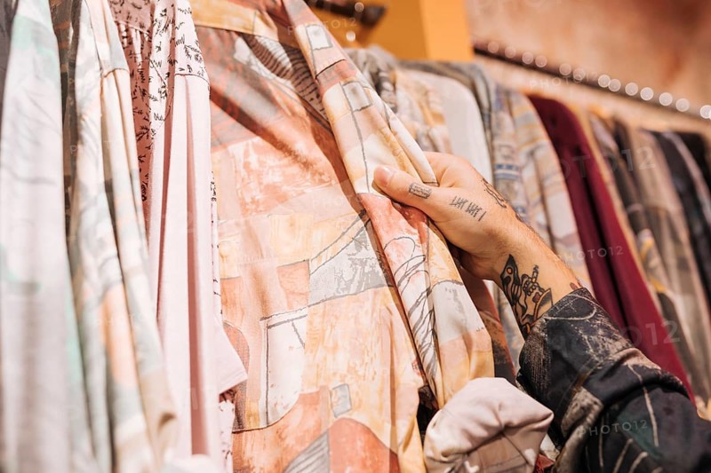 Close up male customer s hand choosing shirt hanging rail shop