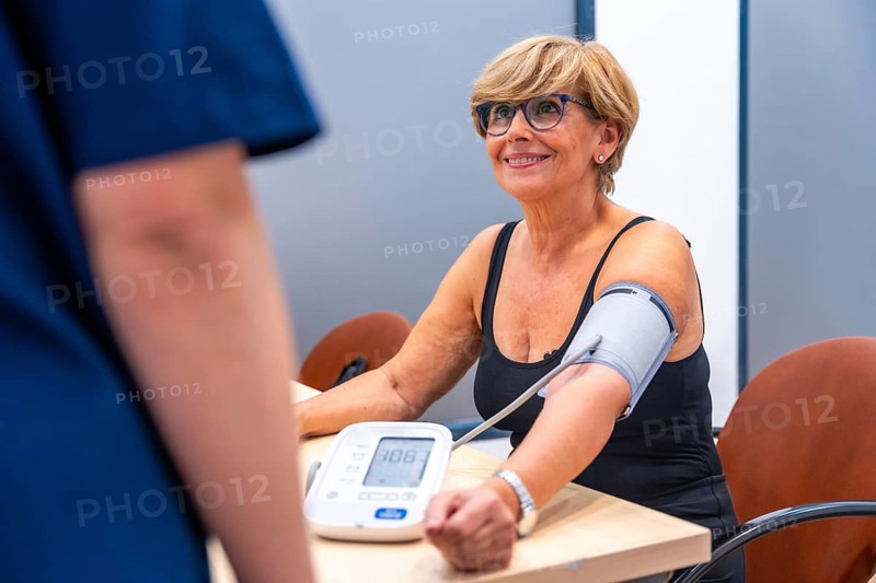 Smiling mature woman sitting during a blood pressure exam in a cardiology clinic