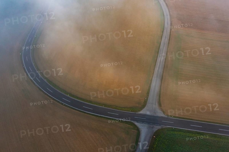 Drone view of a rural landscape shrouded in dense morning fog with a road junction near Prambachkirchen
