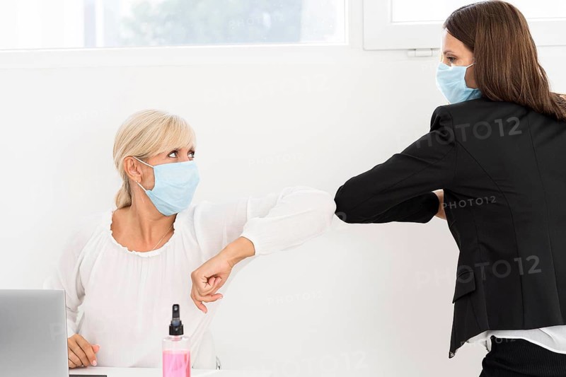 Coworkers wearing masks elbow bump each other