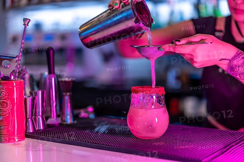 Cropped close-up photo of a woman mixing ingredients of a cocktail in the counter of a nightclub