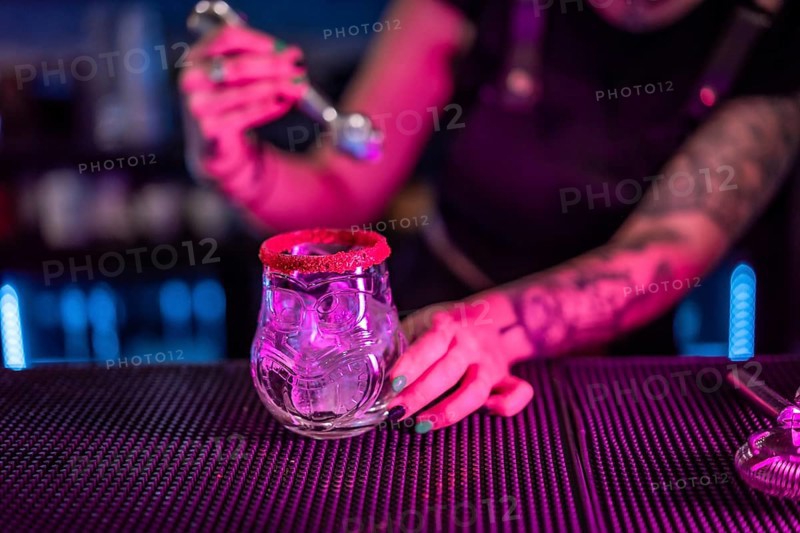 Close-up of a bartender preparing a margarita cocktail adding ice in the counter of a bar with neon lights