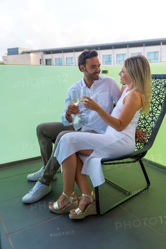 Vertical photo of two lovers sitting on a chair and drinking champagne outdoors in a luxury hotel