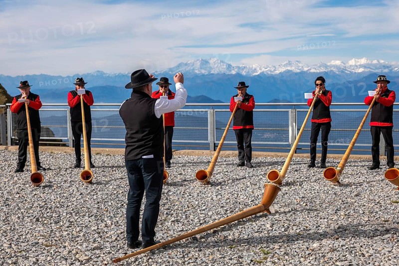 Group of Musicians Playing on Horns of the Alps with Mountainscape and View over Snow Capped Monte Rosa in a Sunny Day in Monte Generoso