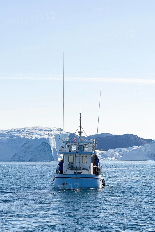 An excursion boat in the UNESCO World Heritage Ilulissat Icefjord sails towards a huge iceberg. Ilulissat