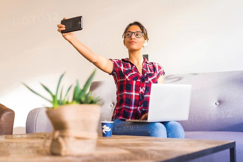 Freelancer taking a selfie while working at home using laptop sitting on a sofa