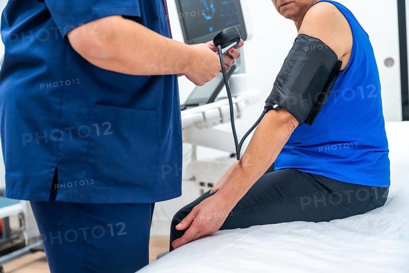 Doctor measuring the blood pressure of a woman sitting on a stretcher in a clinic room