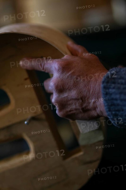 Luthier artisan violin maker wrinkled hand hold carve sculpt chisel ribs of a new classical model cello in workshop Cremona Italy
