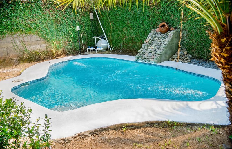 Homemade swimming pool in a garden. Swimming pool designs for the home. Crystal water home pool surrounded by a garden. Home swimming pool maintenance concept