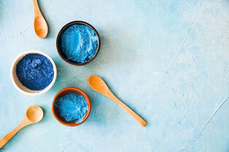 Bowls with holi color powder wooden spoon painted background