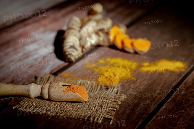 Wooden spoon with turmeric powder background fresh turmeric root out of focus