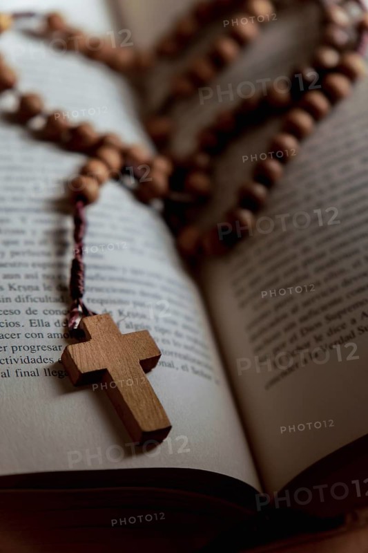 Rosary with a wooden christian cross on a bible with open pages