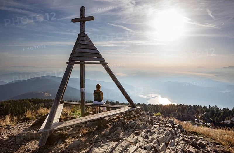 Hiker sitting at the Berger Alm weather cross on the Gerlitzen
