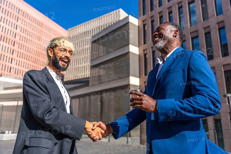 Multi-ethnic business people in suit shaking hands to secure a deal outside a financial building in a sunny day