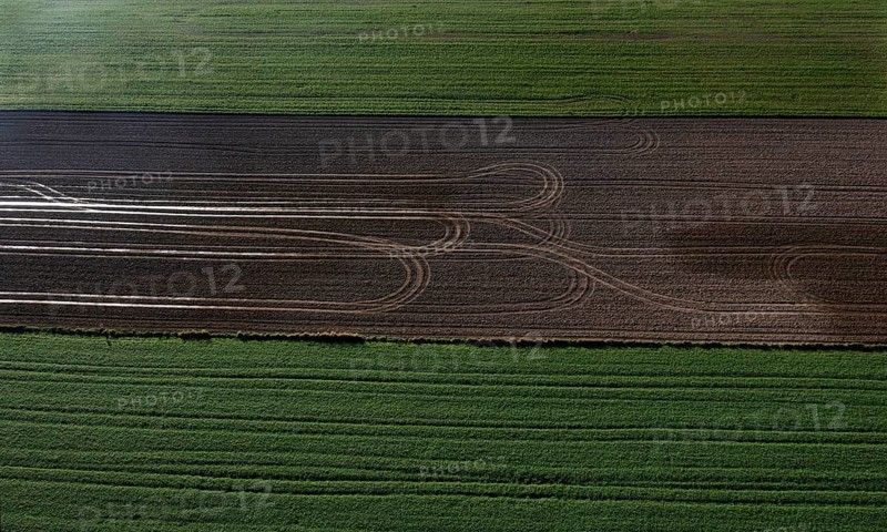 Drone view of green and ploughed fields with tyre tracks