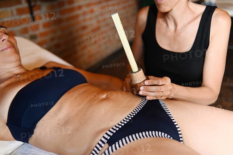 Therapist apply abdominal moxibustion chinese smoking stick moxa medicine burn mugwort in acupuncture point to caucasian adult fit woman to facilitate blood flow and general health through qi oriental meridian point