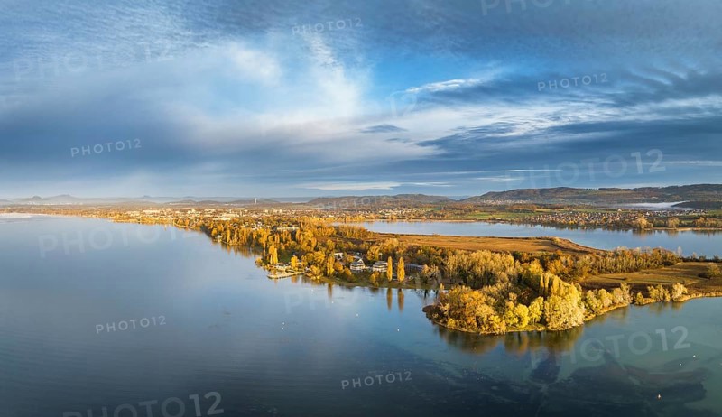 Aerial panorama of the Mettnau peninsula in western Lake Constance illuminated by the morning sun with the spa centre