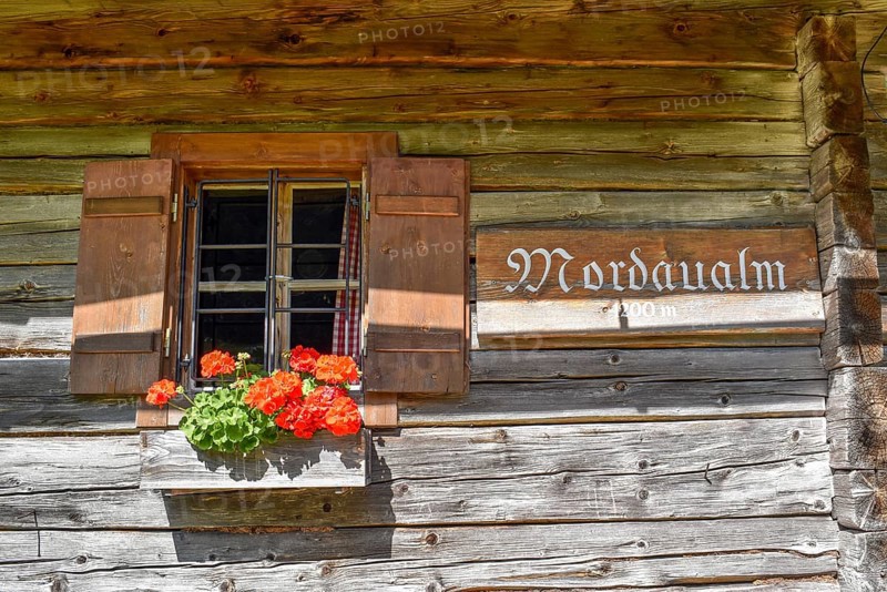 Window of the Mordaualm alpine hut with shutters and geraniums