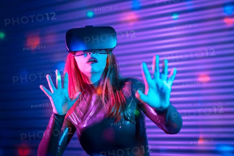Shocked wman during an interactive game with VR goggles in an urban night space with neon lights