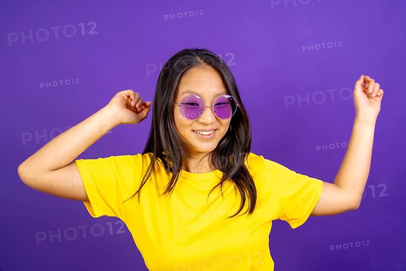 Studio photo with purple background of a chinese woman with sunglasses dancing and smiling
