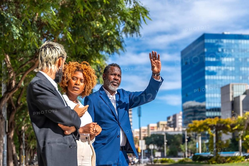 Multi-ethnic business people waiting for a cab and an african mature businessman gesturing to stop one in the city