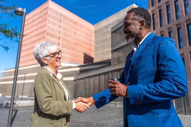 Mature businesswoman and african businessman securing a deal shaking hands outdoors