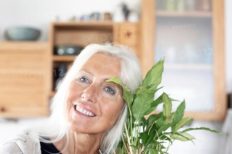 Elderly woman with long hair snuggles up to houseplant at home