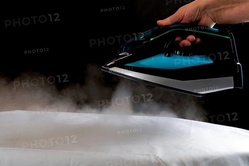 Woman ironing a white cloth by pouring steam from the iron on a black background