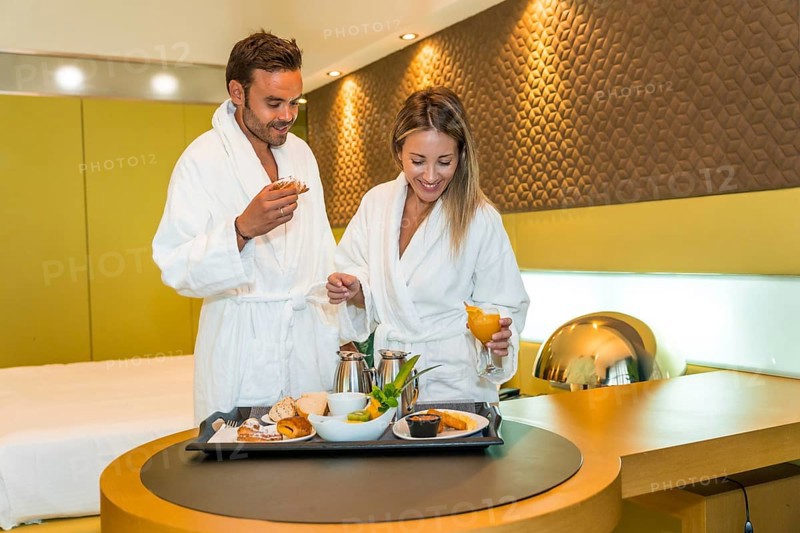 Happy newlywed couple wearing bathrobe eating breakfast in a luxury hotel room