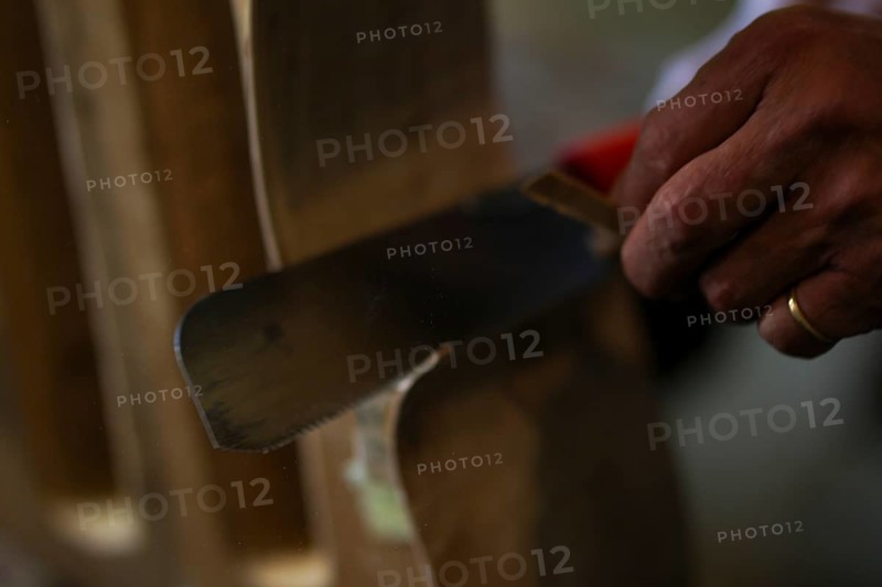 Senior violinmaker holding a tool chisel in workshop in Cremona