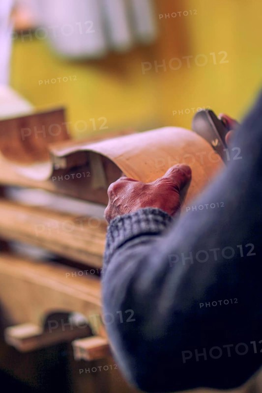 Wrinkled hands of senior Luthier artisan violin maker carve sculpt chisel ribs of a new classical model cello in workshop Cremona Italy