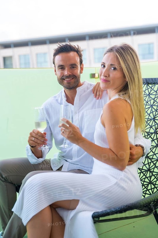 Vertical portrait of lovers celebrating love with champagne sitting on a chair in the terrace of an hotel