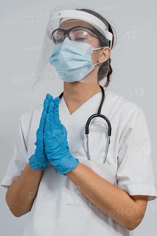 Female doctor with medical mask face shield praying