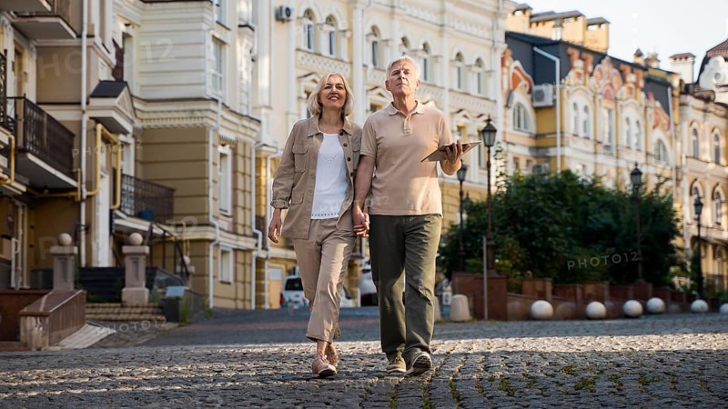 Front view elder couple out walk city with tablet