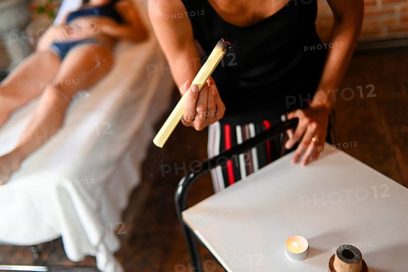 Therapist prepare burning mugwort or moxa herb to apply to 50s adult fit caucasian female patient to facilitate healing and blood flow