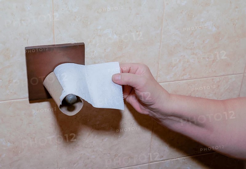 A woman's hand tries to reach for toilet paper but the roll has run out