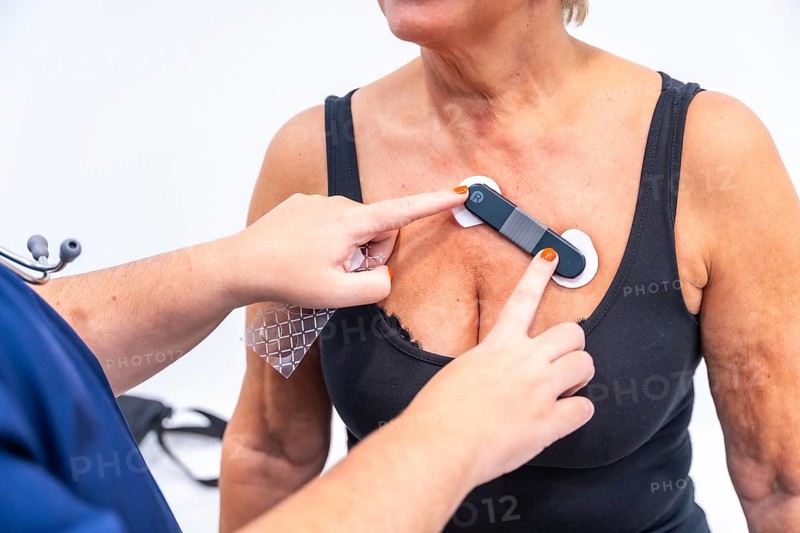 Female doctor putting woman with heart problems undergoing ECG Holter monitor test with innovative device on chest