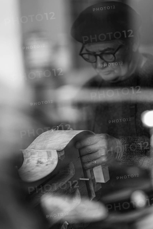 Senior expet luthier artisan violinmaker carve chisel rib of new classic cello in workshop Cremona Italy