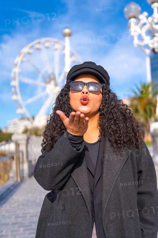 Vertical portrait of a latin stylish woman blowing a kiss standing in the city in a sunny day of winter